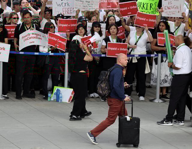 A passenger walks as striking Air Canada flight attendants hold placards as they defy a back to work order at Vancouver International Airport in Richmond, British Columbia, Canada August 18, 2025. REUTERS/Chris Helgren/File Photo