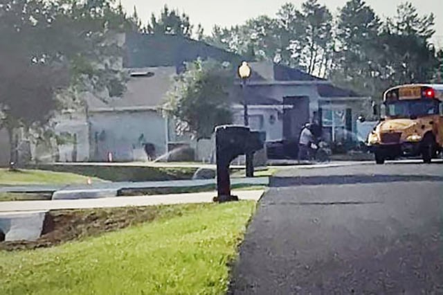 A man pushes a student in a wheelchair towards a school bus moments after sprinklers were activated following the arrival of the bus in Ocala, Fla.