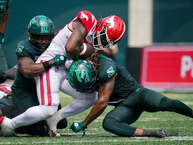 Calgary Stampeders running back Dedrick Mills (26) is tackled by Saskatchewan Roughriders linebacker A.J. Allen (32) and linebacker CJ Reavis (1) during the first half of CFL football action in Regina, on Saturday, July 12, 2025.