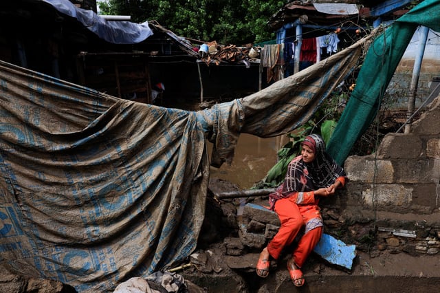 A girl sits outside of her family home, which was damaged following heavy rains and flooding in Pacha Kalay Bazar, in Buner district, Pakistan, on August 18, 2025.