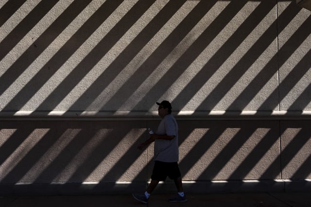 A person walks through the shade along a wall patterned by sunlight in Norwalk, Calif., Tuesday, Aug. 19, 2025. (AP Photo/Jae C. Hong)