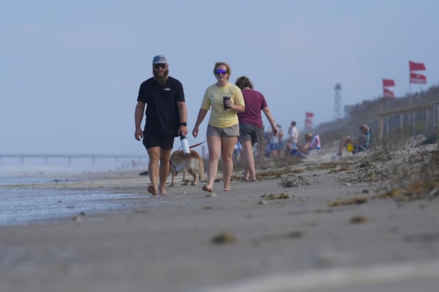 People walk along the beach as waves as red flags, indicating swimming is prohibited, are raised at the beach in Duck, N.C., Tuesday, Aug. 19, 2025, as precautions are taken ahead of Hurricane Erin. (AP Photo/Pablo Martinez Monsivais)