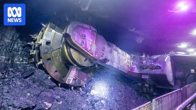 An underground scene showing a wall of coal and mining machinery.