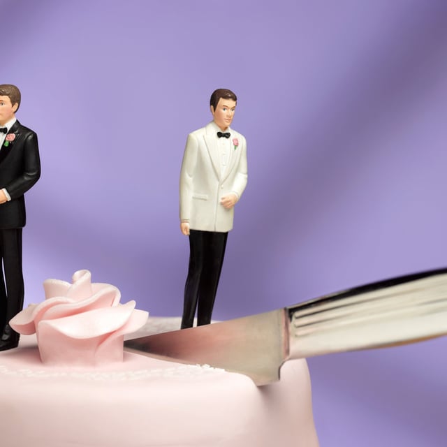 two grooms on wedding cake separated by knife cutting into cake