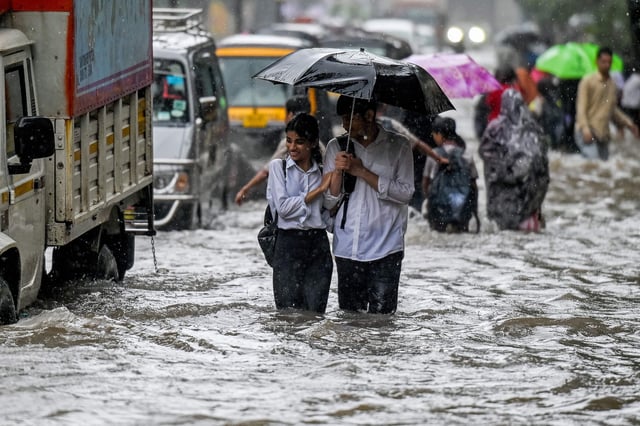 La gente camina por una calle inundada durante fuertes lluvias en Bombay el 18 de agosto de 2025.