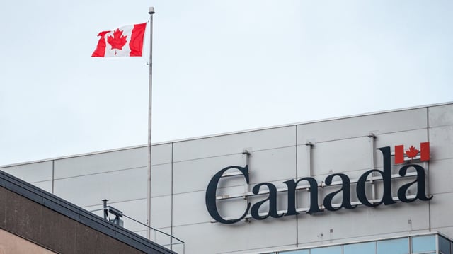 OTTAWA, CANADA - NOVEMBER 10, 2018: Canada Wordmark, the official logo of the Canadian government, on an administrative building next to a Canadian flag waiving