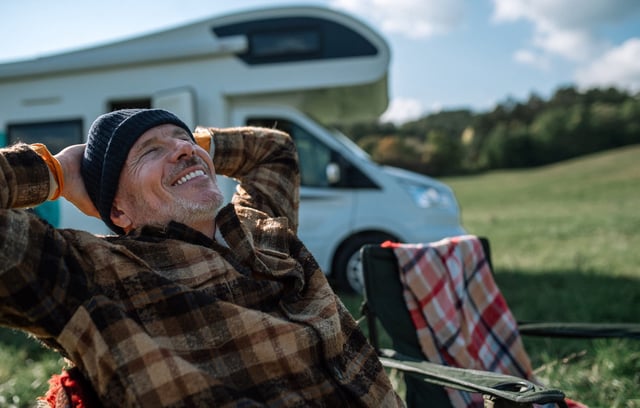 Happy senior man sitting and camping in front of camper.