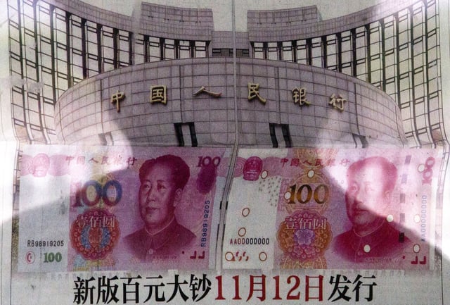 FILE - In this Aug. 11, 2015 photo, a shadow of a man is reflected on a glass as he reads a newspaper reporting China's central bank or People's Bank of China announced the 2015 edition of the 100 renminbi notes will be issued starting from November 12, at a stand in Beijing. (AP Photo/Andy Wong, File)