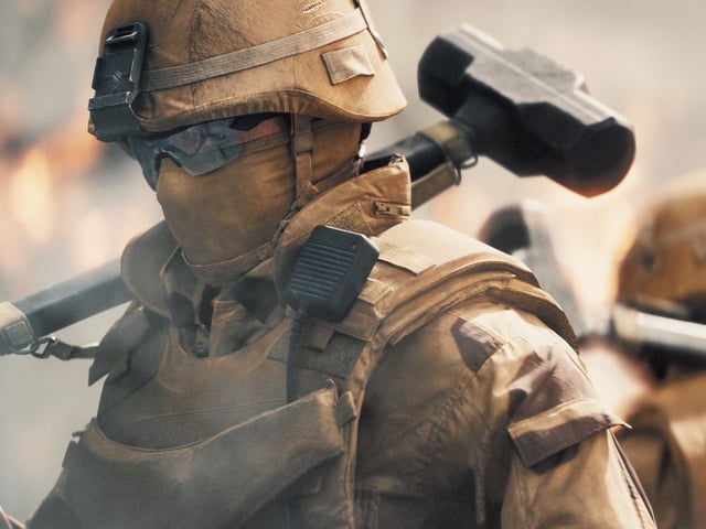 Battlefield 6: A soldier wearing a tan uniform, including a helmet, glasses, and mask, facing to the side with a sledgehammer over their shoulder while turning to look at the camera.
