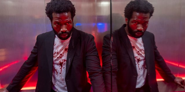 Sope Dirisu in a mirrored elevator with blood on his shirt, in Gangs of London.