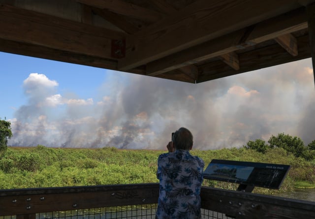A person looks out as smoke billows from a brushfire in the Everglades on Aug. 20, 2025 in Everglades, Florida. Roughly 2,000 acres are burning between two brush fires according to the Florida Forest Service, but currently no structures are reported in danger.