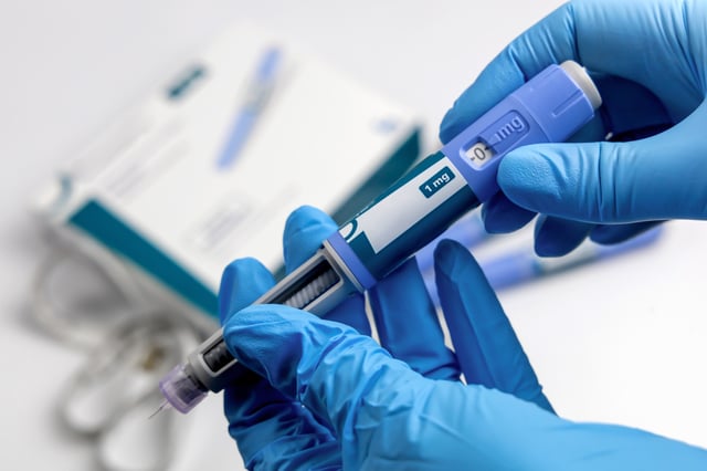 Hands in blue surgical gloves holding Ozempic injection pen.