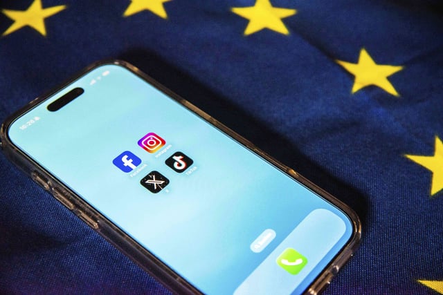 29 July 2025, Belgium, Brüssel: The logos of Facebook, Instagram, X and Tiktok can be seen on a smartphone lying on an EU flag