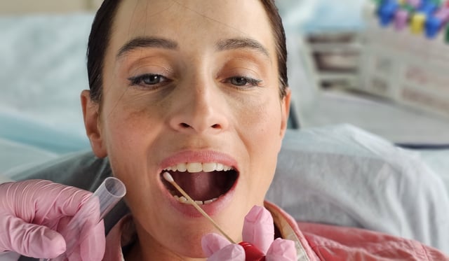 Clinician's hands taking mouth swab of woman.