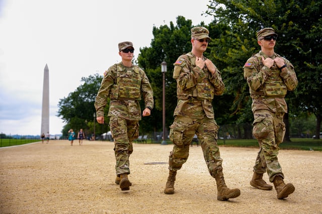 The Washington Monument is visible as National Guard troops walk along the National Mall on August 20, 2025 in Washington, DC.