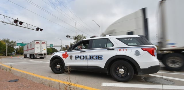 A police vehicle is on the scene as trucks make their way to the Ambassador Bridge border crossing in Windsor, Ont., Monday, Oct.4, 2021. THE CANADIAN PRESS/Rob Gurdebeke