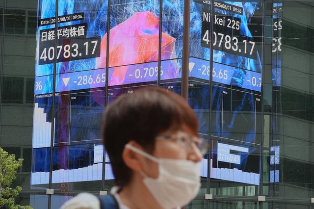 A person stands in front of an electronic stock board showing Japan's Nikkei index at a securities firm Friday, Aug. 1, 2025, in Tokyo. (AP Photo/Eugene Hoshiko)