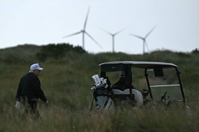 President Donald Trump, backdropped by wind turbines at the European Offshore Wind Deployment Centre, also known as the Aberdeen Bay Wind Farm, walks on the first fairway after playing off the first tee to officially open the Trump International Golf Links course in Balmedie, Aberdeenshire, north east Scotland on July 29, 2025.