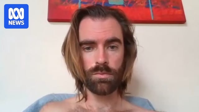 A close-up shot of a shirtless man with long brown hair and a beard, with a weary look while appearing on a video call.