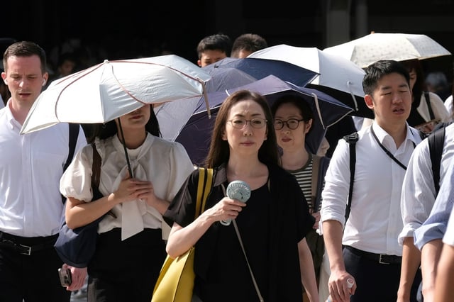 Une femme se rend au travail avec un ventilateur miniature à la main par une matinée chaude et ensoleillée à Tokyo, le 6 août 2025