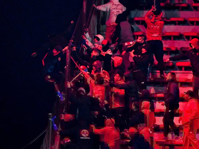 A Universidad de Chile fan lets go of a fence while another clings to it as they try to escape clashes with Independiente supporters during the second leg of the Copa Sudamericana Round of 16 match, which was suspended due to violence in the stands, with the Chilean side leading on aggregate, in Avellaneda, Argentina August 20, 2025. REUTERS/Facundo Morales