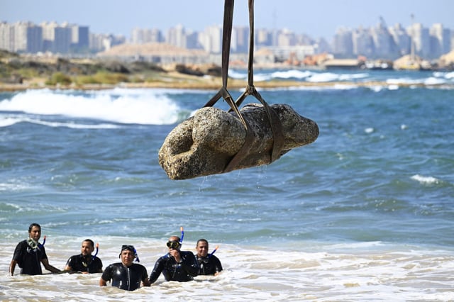 Divers watch as a crane pulls a piece of stone from the waters.          