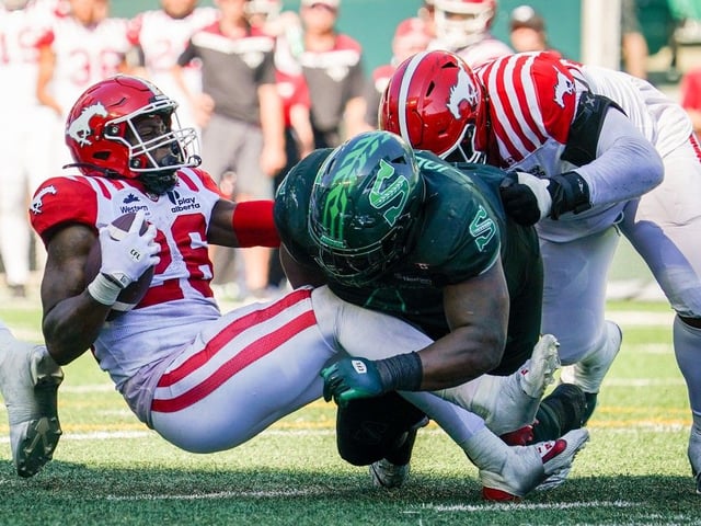 Calgary Stampeders running back Dedrick Mills (26) is tackled by Saskatchewan Roughriders defensive lineman Micah Johnson (4) during the second half of CFL football action in Regina, on Saturday, July 12, 2025.