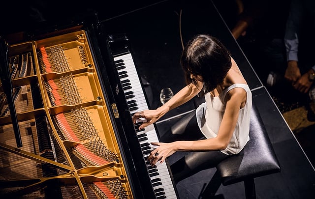 An overhead view of a woman with dark hair and a white top playing a concert piano.