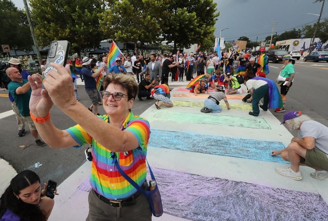 Orlando City Commissioner Patty Sheehan, left, smiles as she takes a selfie during a protest at a crosswalk in front of the former Pulse nightclub in Orlando on Thursday, August 21, 2025. The crosswalk had been painted in rainbow-themed colors, but overnight Wednesday, the rainbow-colored paint was removed from the crosswalk by the Florida Department of Transportation in an ongoing effort to remove “political banners” from public roadways. This sparked outrage from the LGBTQ+ community. During Thursday’s protest, demonstrators “replaced” the rainbow colors on the crosswalk using chalk. The former Pulse gay nightclub is now a memorial site for the 49 victims who were murdered there in 2016. (Stephen M. Dowell/Orlando Sentinel)
