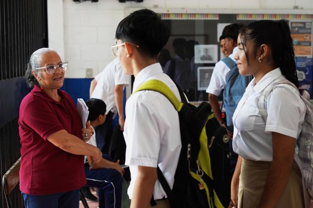 Una maestra saluda a los estudiantes que llegan a clase en una escuela pública mientras verifica que su cabello y uniformes cumplan con las reglas en San Salvador, El Salvador, el viernes 22 de agosto de 2025. (AP Foto/Salvador Meléndez)