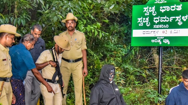 Security personnel with the whistleblower, who claims to have been coerced into burying and cremating bodies of women and minors, near a site of an alleged burial related to the Dharmasthala mass burial case, at Dharmasthala, in Dakshina Kannada district, 