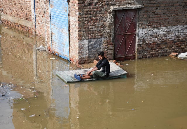 A man sits on a wooden table along a flooded street after the rain at Latifabad, Hyderabad, Pakistan, August 22, 2025. REUTERS/Yasir Rajput