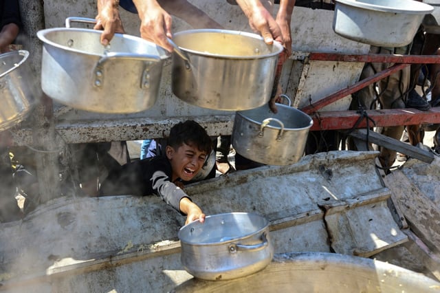 Un garçon palestinien tend une casserole vide devant une organisation de charité locale distribuant du riz cuit, dans la ville de Gaza, le 23 août 2025