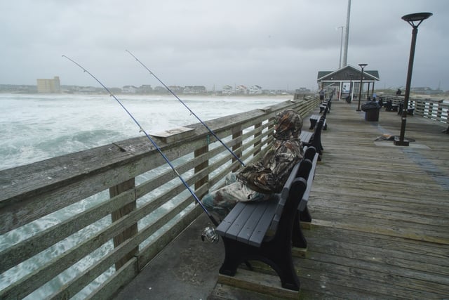 Sebastian Kettner fishes on Jennette's Pier as waves from Hurricane Erin crash ashore in Nags Head, N.C., Thursday, Aug. 21, 2025. (AP Photo/Allen G. Breed)