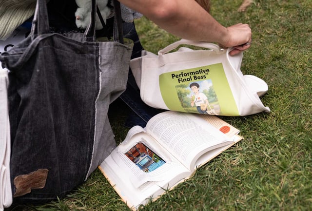 Steven Zhang reveals a cutout for his phones in a book after receiving a tot bag for placing top five during a performative male contest at Alamo Square Park in San Francisco.