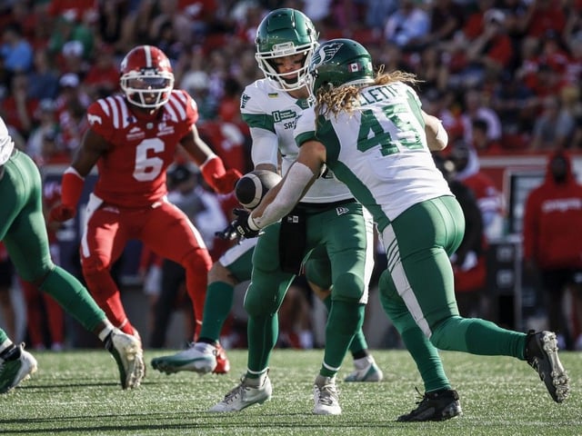 Saskatchewan Roughriders quarterback Trevor Harris, centre, hands the ball off to A.J. Ouellette, right, as Calgary Stampeders' Derrick Moncrief looks on during first half CFL football action in Calgary, Saturday, Aug. 23, 2025.