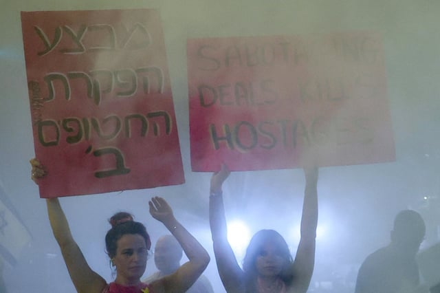 Des manifestants brandissent des pancartes au milieu des fumées d'extincteurs lors d'une manifestation organisée par les familles des Israéliens retenus en otages dans la bande de Gaza, devant le ministère de la Défense à Tel-Aviv, le 23 août 2025