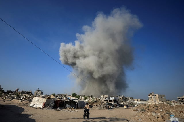 A Palestinian man rides a bike as smoke rises following an Israeli strike, in Gaza City, August 24, 2025. REUTERS/Dawoud Abu Alkas