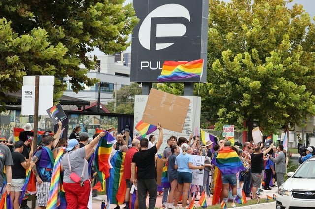 Demonstrators wave flags and cheer during a protest at a crosswalk in front of the former Pulse nightclub in Orlando on Thursday, August 21, 2025. The crosswalk had been painted in rainbow-themed colors, but overnight Wednesday, the rainbow-colored paint was removed from the crosswalk by the Florida Department of Transportation in an ongoing effort to remove “political banners” from public roadways. This sparked outrage from the LGBTQ+ community. During Thursday’s protest, demonstrators “replaced” the rainbow colors on the crosswalk using chalk. The former Pulse gay nightclub is now a memorial site for the 49 victims who were murdered there in 2016. (Stephen M. Dowell/Orlando Sentinel)