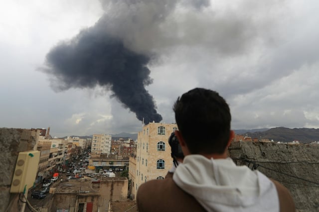 Un journaliste prend une photo de la fumée noire qui s'élève après une frappe israélienne sur Sanaa, la capitale du Yémen tenue par les rebelles houthis, le 24 août 2025