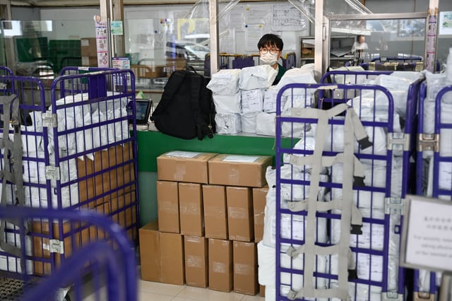 TOPSHOT - Stacked parcels are seen up front as a Hongkong Post employee stands at a service counter at a post office in Hong Kong on April 16, 2025. Hong Kong's postal service said April 16 it will stop shipping goods bound for the United States in response to "bullying" tariff hikes by US President Donald Trump. Hongkong Post will stop accepting surface mail of US-bound items with immediate effect and air mail items starting from April 27. (Photo by Peter PARKS / AFP) (Photo by PETER PARKS/AFP via Getty Images)          