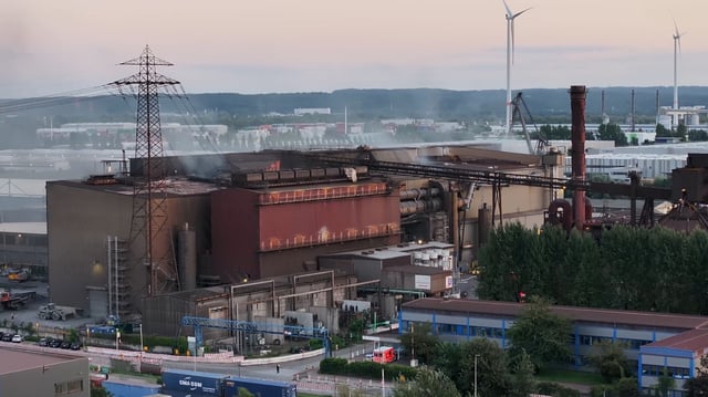 Im Hamburger Werk von ArcelorMittal in Waltershof sollen große Mengen flüssiger Stahl ausgelaufen sein. Rauch dringt aus dem Hallendach.