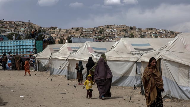 Frauen und Kinder gehen an Zelten in einem Flüchtlingscamp vorbei