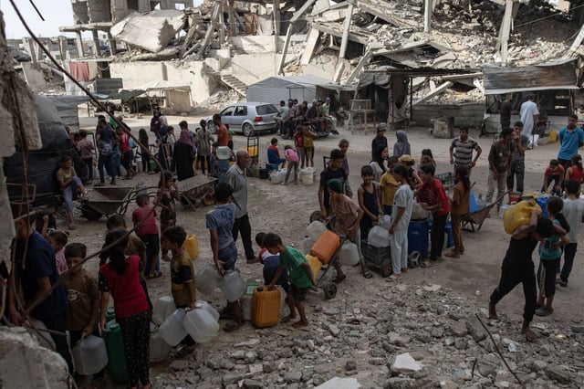 Decenas de ciudadanos palestinos desplazados esperan para llenar contenedores con agua potable.