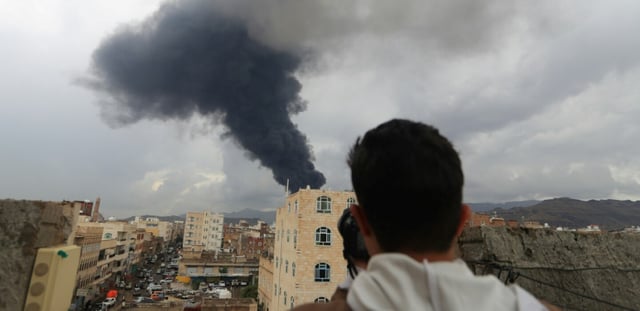 Un journaliste prend une photo de la fumée noire qui s'élève après une frappe israélienne sur Sanaa, la capitale du Yémen tenue par les rebelles houthis, le 24 août 2025