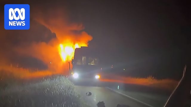 A bus engulfed in flames as seen from side of road at night.