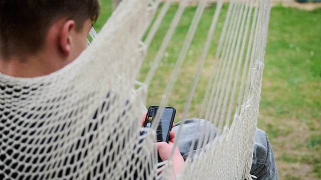 Ein Jugendlicher sitzt mit Smartphone in der Hängematte.