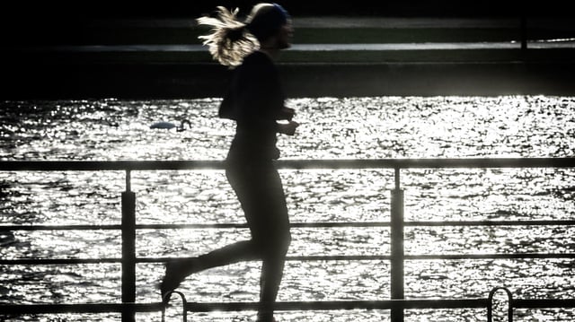 Eine Joggerin läuft am Ufer entlang.
