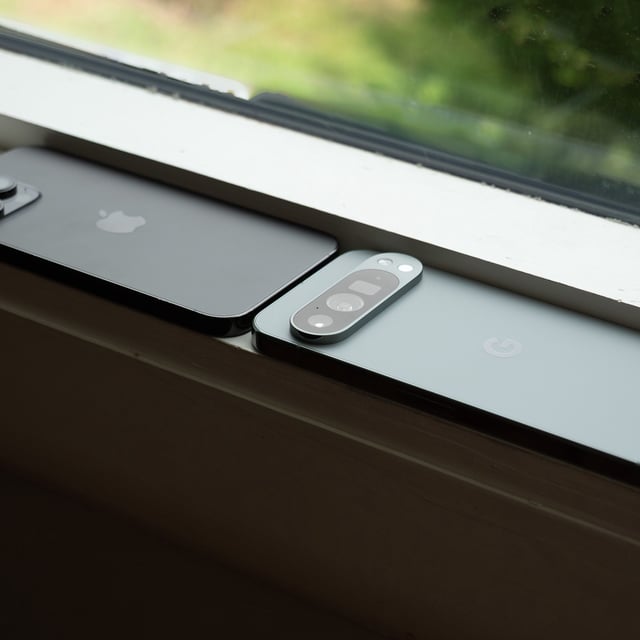 An Apple iPhone 14 Pro Max next to a Google Pixel 9 Pro XL on a windowsill