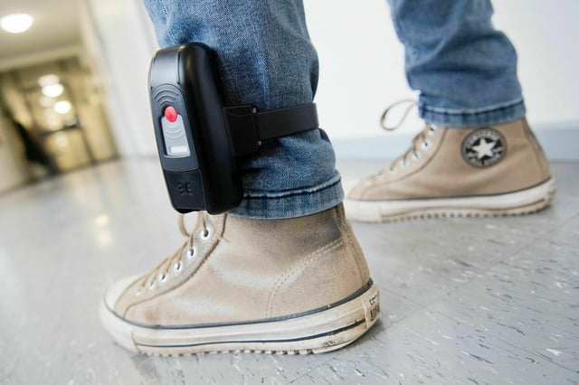 Ein Mann trägt eine elektronische Fussfessel über seiner Jeans